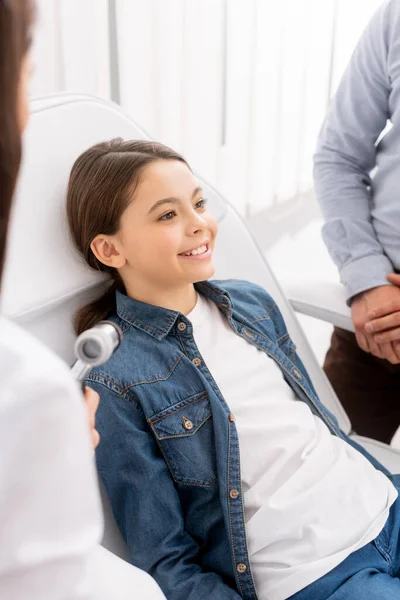 Selective focus of smiling child near father and ent physician with otoscope — Stock Photo