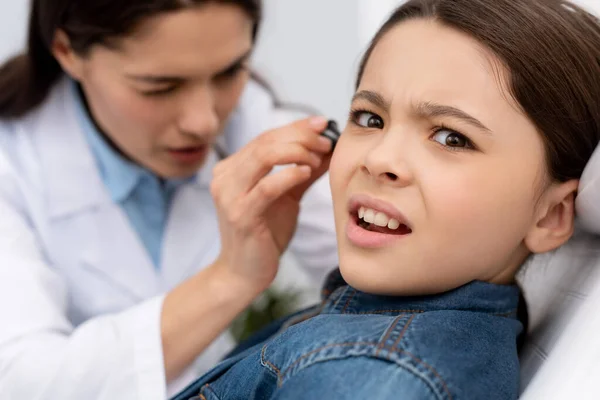 Foco selectivo del otorrinolaringólogo atento que examina el oído del niño asustado - foto de stock