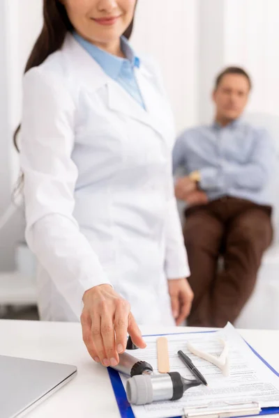 Vista recortada del médico sonriente tomando otoscopio, y paciente sentado en silla médica en el fondo - foto de stock