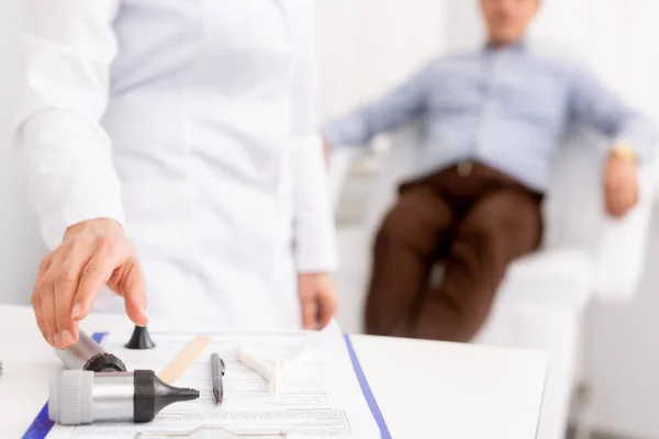 Orientation sélective du médecin traitant qui prend un otoscope et du patient assis sur une chaise médicale sur fond — Photo de stock