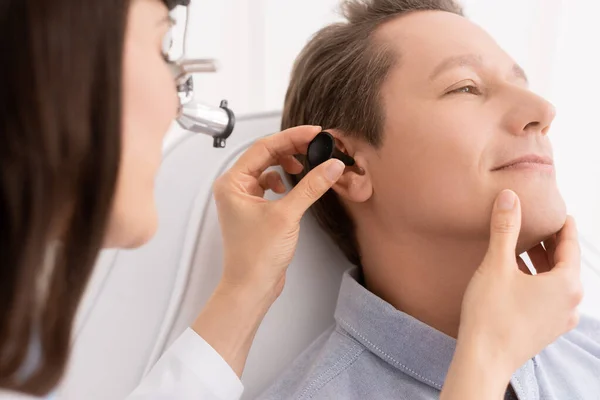 Vue recadrée de otolaryngologue dans le phare ent examinant l'oreille du beau patient — Photo de stock