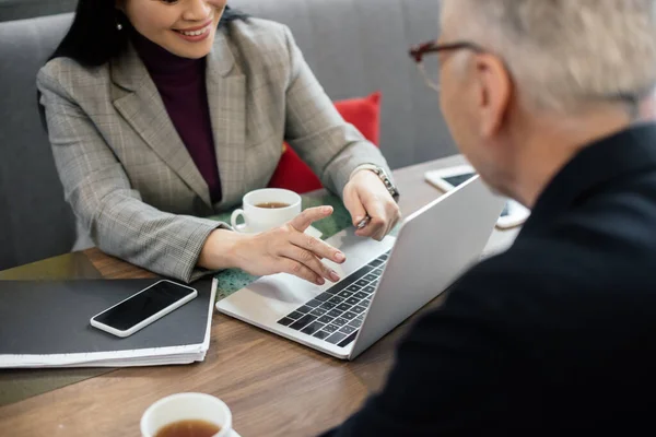 Vue recadrée d'une femme d'affaires souriante utilisant un ordinateur portable et parlant avec un homme d'affaires lors d'une réunion d'affaires — Photo de stock