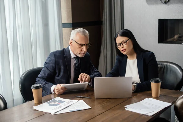 Businessman and asian businesswoman looking at laptop and talking during business meeting — Stock Photo
