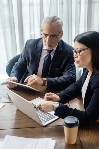 Hombre de negocios y mujer de negocios asiática mirando el ordenador portátil y hablando durante la reunión de negocios - foto de stock