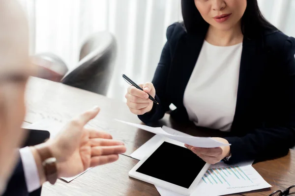 Abgeschnittene Ansicht eines Geschäftsmannes, der mit der Hand zeigt, und einer Geschäftsfrau, die während eines Geschäftstreffens Papier betrachtet — Stockfoto