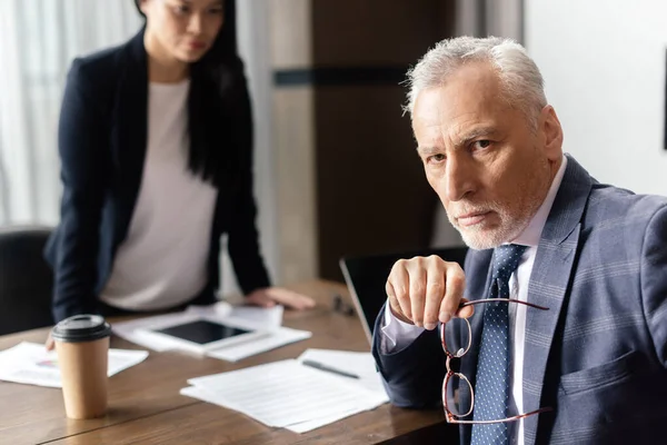 Selective focus of businessman looking at camera and asian businesswoman on background during business meeting — Stock Photo
