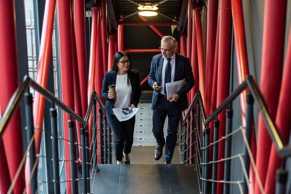 Hochwinkelaufnahme eines lächelnden Geschäftsmannes und einer asiatischen Geschäftsfrau, die auf Treppen reden und gehen — Stockfoto