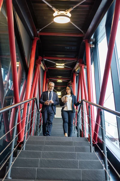 Niederwinkelaufnahme von Geschäftsmann und asiatischer Geschäftsfrau, die auf Treppen reden und gehen — Stockfoto