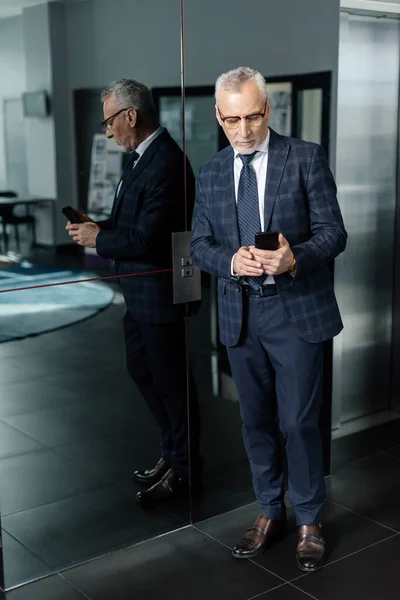 Homem de negócios de terno usando smartphone e de pé perto do elevador — Fotografia de Stock