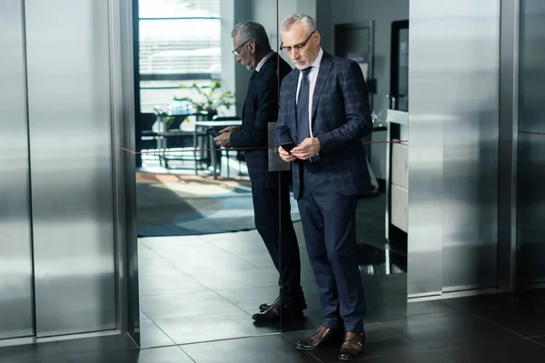 Businessman in suit using smartphone and standing near elevator — Stock Photo