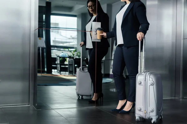 Cropped view of asian businesswoman with travel bag pushing button of elevator — Stock Photo
