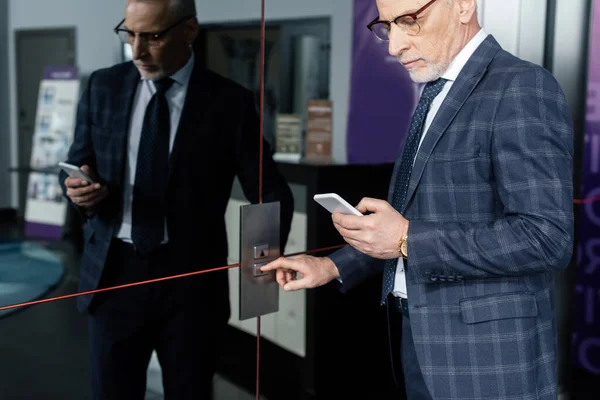 Vue recadrée de l'homme d'affaires en utilisant smartphone et bouton poussoir de l'ascenseur — Photo de stock