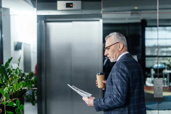 Seitenansicht eines Geschäftsmannes, der Zeitung liest und Pappbecher hält — Stockfoto