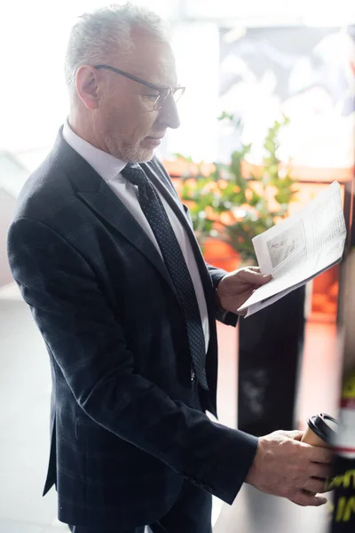 Vue de côté de l'homme d'affaires lisant le journal et tenant la tasse en papier — Photo de stock