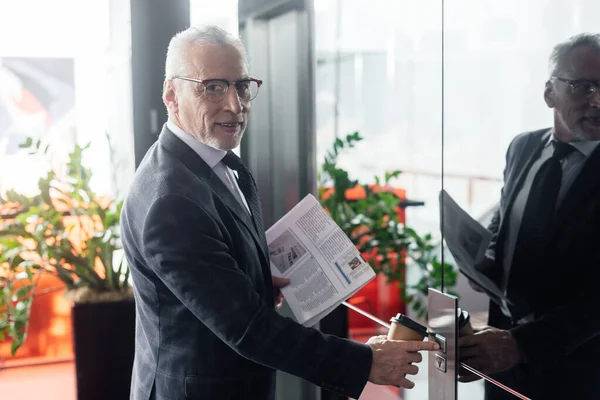 Lächelnder Geschäftsmann mit Zeitung und Pappbecher drückt Taste des Fahrstuhls — Stockfoto