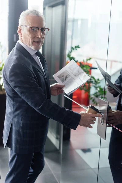 Homme d'affaires souriant avec papier et journal tasse bouton-poussoir de l'ascenseur — Photo de stock