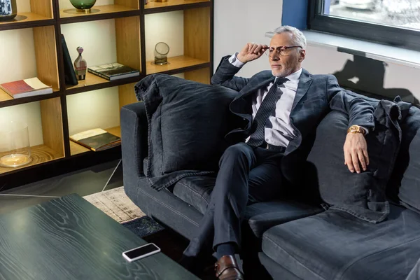 Vista de ángulo alto del hombre de negocios en traje sentado en el sofá y mirando hacia otro lado - foto de stock