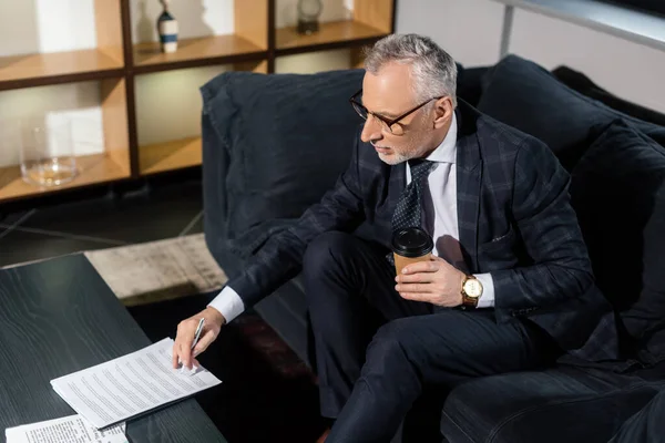 Vista de ángulo alto del hombre de negocios sosteniendo taza de papel y papel de firma - foto de stock