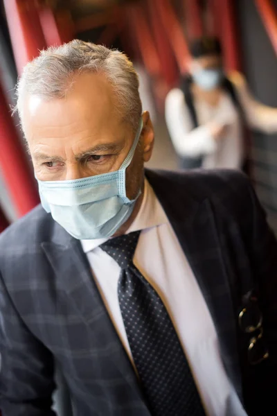 Бізнесмен в офіційному одязі з медичною маскою, дивлячись подалі — стокове фото