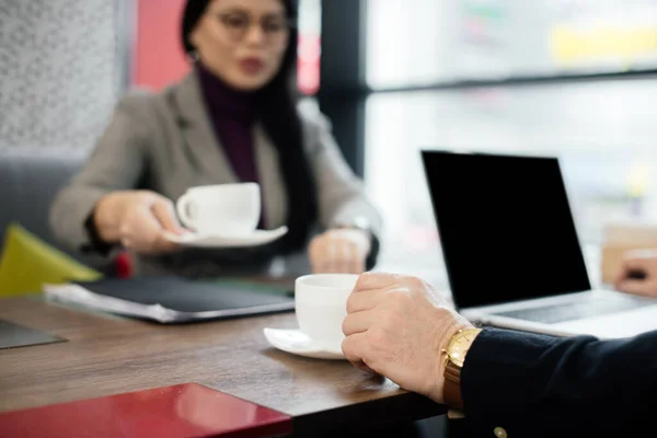 Vista cortada de empresário e asiático empresária sentado à mesa e segurando copos — Fotografia de Stock