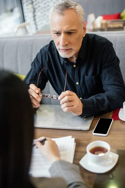 Foco seletivo do empresário segurando óculos e conversando com empresária no café — Fotografia de Stock