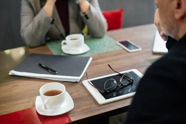 Vista recortada de hombre de negocios y mujer de negocios sentado a la mesa en la cafetería - foto de stock