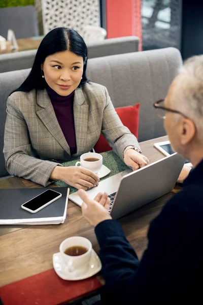 Enfoque selectivo de mujer de negocios asiática hablando con hombre de negocios en la cafetería - foto de stock