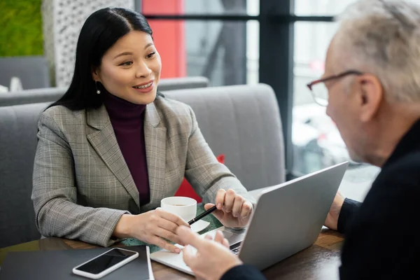 Foyer sélectif de sourire asiatique femme d'affaires parler avec un homme d'affaires dans le café — Photo de stock