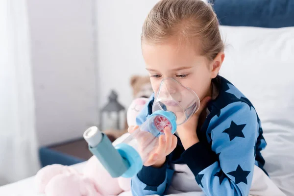 Niño enfermo usando inhalador con espaciador en el dormitorio - foto de stock