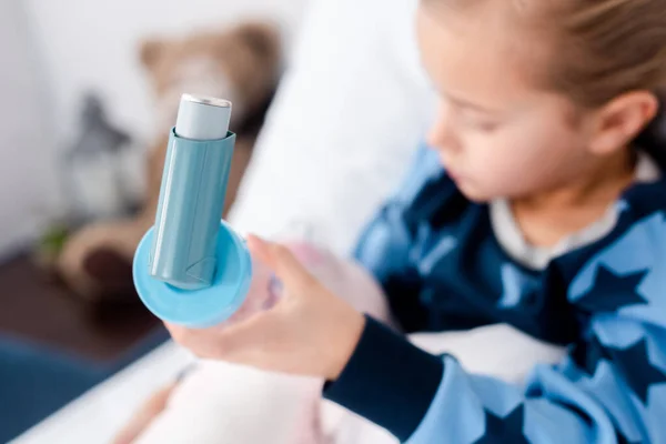 Enfoque selectivo del niño enfermo sosteniendo inhalador con espaciador en el dormitorio - foto de stock
