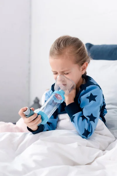 Asthmatic child with closed eyes using inhaler with spacer — Stock Photo