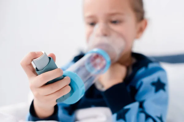 Enfoque selectivo del niño asmático utilizando inhalador con espaciador en casa - foto de stock