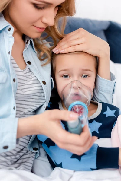 Selective focus of attractive mother holding inhaler with spacer near sick daughter — Stock Photo
