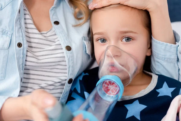 Selective focus of caring mother holding inhaler with spacer near sick daughter — Stock Photo