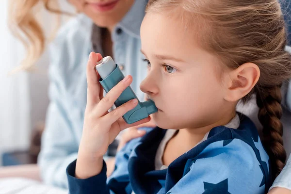 Concentrazione selettiva del bambino malato utilizzando l'inalatore vicino alla madre premurosa a casa — Foto stock