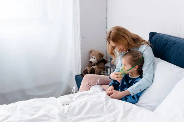 Mère toucher masque respiratoire sur fille asthmatique en utilisant un inhalateur compresseur dans la chambre — Photo de stock