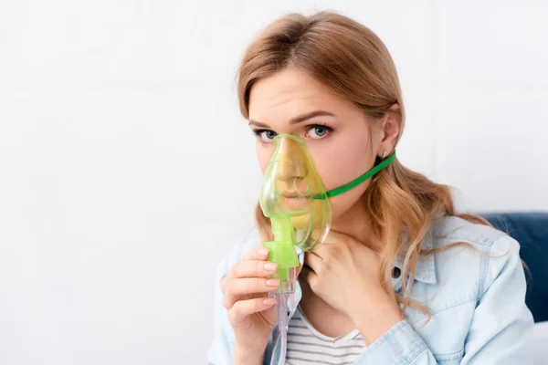 Mujer asmática sosteniendo máscara respiratoria cerca de la cara y mirando a la cámara - foto de stock