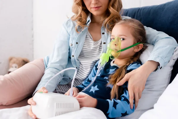 Mother sitting with diseased daughter in respiratory mask using compressor inhaler — Stock Photo