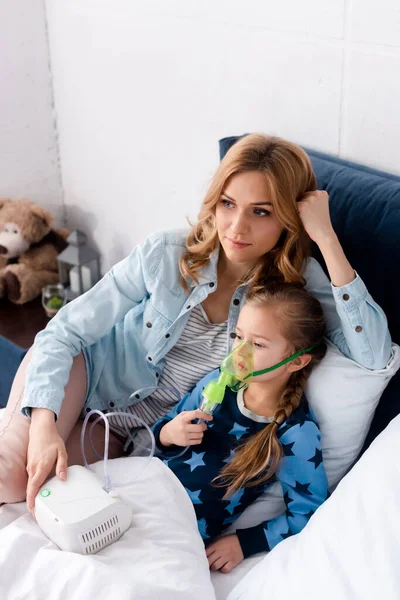 Fürsorgliche Mutter nahe asthmatischer Tochter in Atemmaske mit Kompressor-Inhalator — Stockfoto