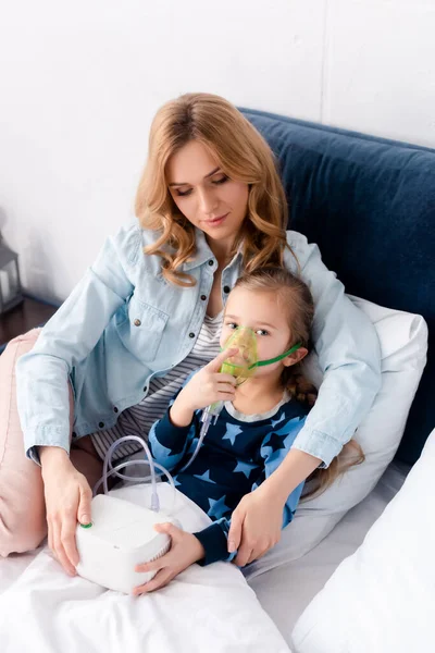 Asthmatisches Kind mit Atemmaske blickt nahe fürsorglicher Mutter in die Kamera — Stockfoto
