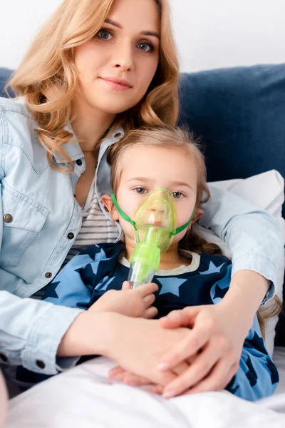 Asthmatisches Kind mit Atemmaske blickt in die Kamera in der Nähe der schönen Mutter — Stockfoto