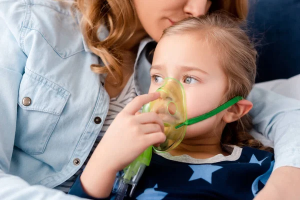 Mãe beijando filha asmática em máscara respiratória — Fotografia de Stock