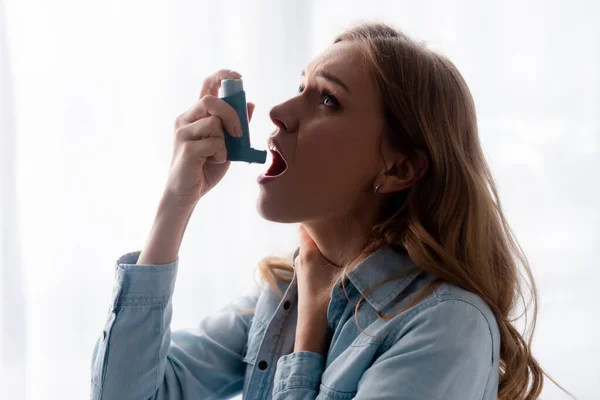 Mujer asmática tocando el cuello y usando inhalador - foto de stock