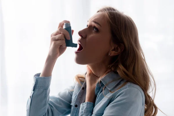 Asthmatic woman touching neck and using inhaler — Stock Photo