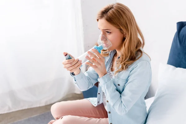 Asthmatic woman using inhaler with spacer in bedroom — Stock Photo