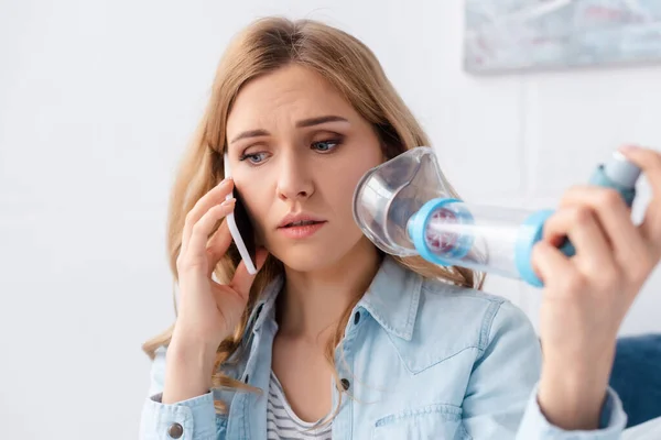 Foco seletivo da mulher asmática segurando inalador com espaçador e falando no smartphone — Fotografia de Stock