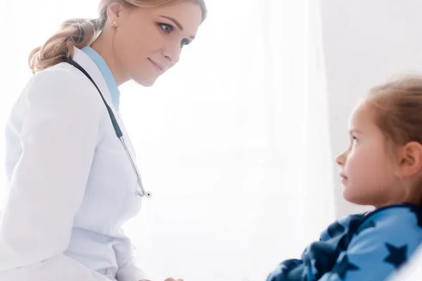 Вибірковий фокус привабливого лікаря в білому пальто, дивлячись на хворого хлопчика — стокове фото