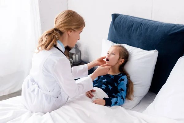 Atractivo médico en blanco abrigo examinar enfermo niño - foto de stock