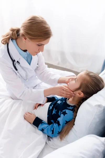 Profile of attractive doctor in white coat examining sick kid — Stock Photo