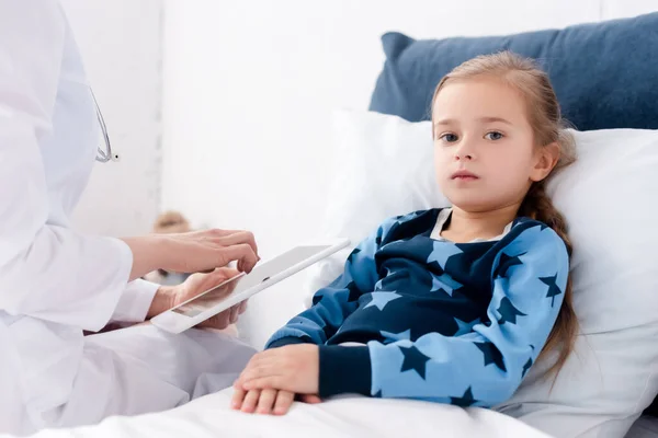 Doctor in white coat holding digital tablet near sick kid — Stock Photo